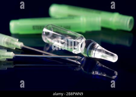 Ampoule de médicament en verre transparent avec deux aiguilles de filtre sur une surface réfléchissante bleue. Banque D'Images