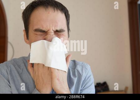 Un jeune homme malade souffrant de grippe à la maison. Un jeune homme éternue dans un chiffon qui ne propagerait pas les germes. Quarantaine à domicile pour les patients atteints du virus. sn Banque D'Images