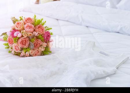 Un beau bouquet de fleurs a été aménagé sur un lit blanc propre. À côté de la robe de mariée ont été placés ensemble. Banque D'Images