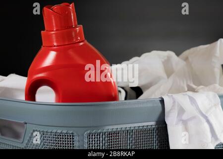 Linge préparé pour le lavage dans un panier avec des moyens de lavage dans une bouteille en plastique rouge. Gros plan. Banque D'Images