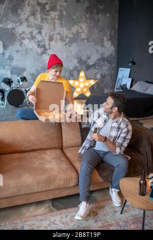 Jeune homme dans un chapeau rouge montrant de la pizza à son ami aux cheveux sombres Banque D'Images