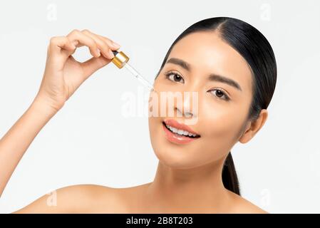 Belle femme asiatique appliquant du sérum hydratant anti-vieillissement sur son visage pour des concepts de beauté et de soins de la peau Banque D'Images