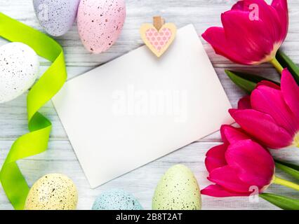 Carte de vœux. Fleurs de tulipes printanières, œufs de pâques et décorations sur fond en bois blanc d'en haut dans un style plat. Banque D'Images