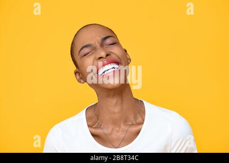 Heureuse femme afro-américaine optimiste riant avec les yeux fermé isolé sur fond jaune coloré Banque D'Images