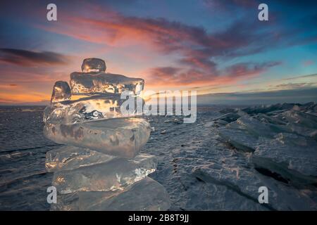 Coucher de soleil reflété dans un grand bloc de glace hummock sur l'arrière-plan du lac gelé. Banque D'Images