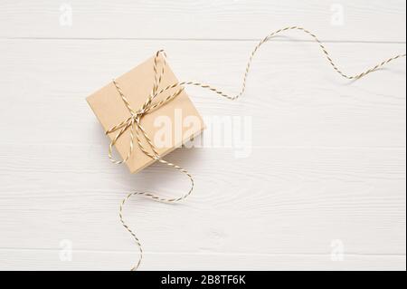 la boîte cadeau sur papier kraft avec un arc de corde est sur une table en bois blanc, avec place pour votre texte Banque D'Images