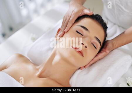 Jeune femme souriante posée sur le dos et se faire masser le visage Banque D'Images