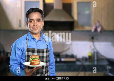 Chef indien masculin avec un hamburger dans une cuisine Banque D'Images