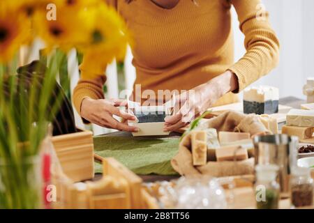 Image rapprochée d'une femme qui emballe du savon parfumé qu'elle a fait à la maison dans une boîte en papier Banque D'Images