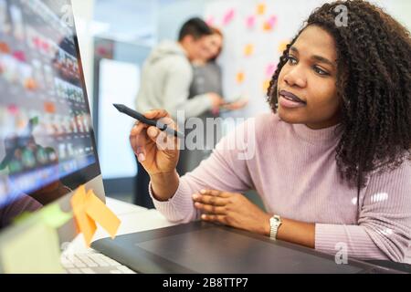 Créateur graphique africain créatif avec stylo pointant vers le moniteur d'ordinateur Banque D'Images