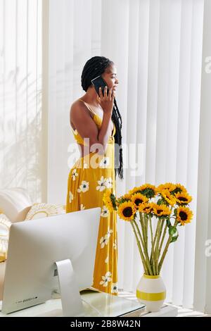 Une femme positive et attrayante qui regarde par la fenêtre lorsqu'elle parle au téléphone Banque D'Images