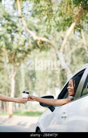 Enchantée, la jeune femme noire qui achète du café en voiture à travers le café Banque D'Images