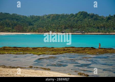 Plage secrète, eau turquoise étonnante et une femme locale marchant à marée basse dans Java ouest, Indonésie Banque D'Images