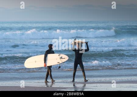 De heureux surfeurs marchant hors de la mer transportant leurs planches de surf à Fistral à newquay en Cornwall. Banque D'Images