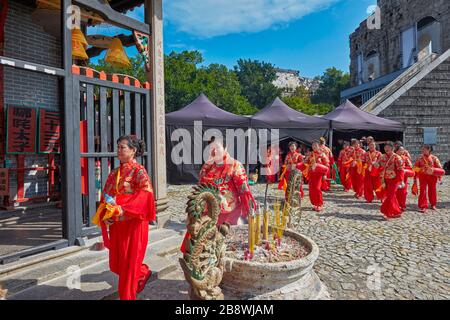 Les femmes locales en costumes traditionnels rouges marchant près du temple Na Tcha. Macao, Chine. Banque D'Images