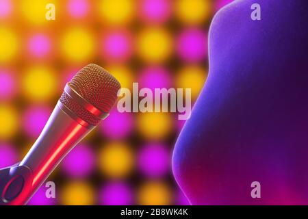 Gros plan de la femme debout à côté du microphone vocal illuminé par des lumières disco en arrière-plan. Musique, chant, discothèque, karaoké et reproduction sonore. Banque D'Images