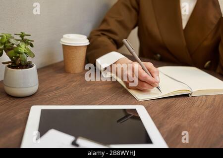 Gros plan sur une femme d'affaires inreconnaissable et mûre écrivant dans le journal tout en étant assis à une table de café en bois, espace de copie Banque D'Images