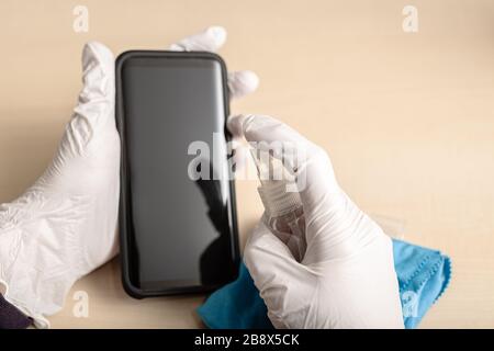 Mains avec gants nettoyer le téléphone portable avec un spray désinfectant. COVID-19 concept de prévention de la contamination par des éclosions de coronavirus. Espace de copie Banque D'Images