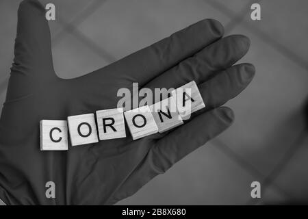 Une main avec un gant sur tient des briques de Scrabble, qui forment le mot: Corona Banque D'Images