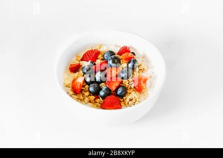 Un petit déjeuner sain et heureux au gruau pour un moment d'isolement. Un bol d'avoine, de granola, de fraise, de bleuets, de yaourt, avec bol blanc, fond blanc Banque D'Images