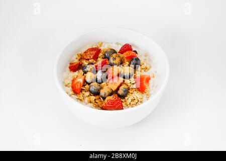 Un petit déjeuner sain et heureux au gruau pour un moment d'isolement. Un bol d'avoine, de granola, de fraise, de bleuets, de yaourt, avec bol blanc, fond blanc Banque D'Images