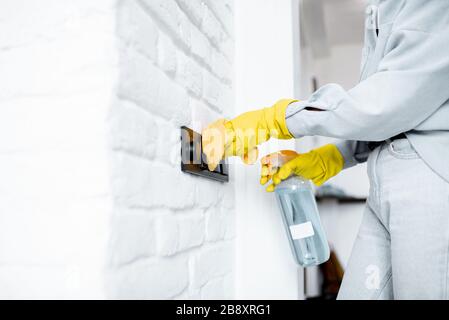 Femme dans des gants de protection désinfectant des commutateurs muraux lors du nettoyage à la maison, vue rapprochée sur les mains Banque D'Images