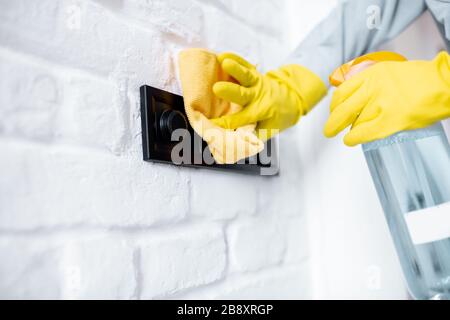 Femme dans des gants de protection désinfectant des commutateurs muraux lors du nettoyage à la maison, vue rapprochée sur les mains Banque D'Images