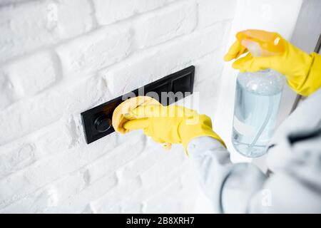 Femme dans des gants de protection désinfectant des commutateurs muraux lors du nettoyage à la maison, vue rapprochée sur les mains Banque D'Images