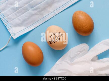 Gants, masque et œufs avec inscription PÂQUES sur fond bleu clair vue de dessus. Pâques pendant le concept de coronavirus. Banque D'Images