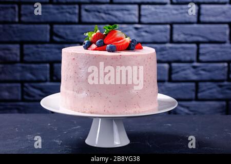 Délicieux et sucré un gâteau de fraise rose entier décoré de fruits frais et de feuilles de menthe sur un stand de gâteau blanc avec un mur de brique à l'arrière-plan Banque D'Images