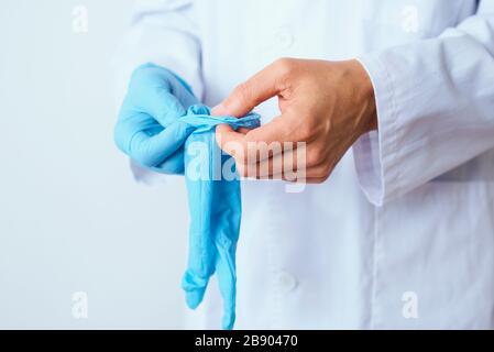 closeupo d'un homme de docteur caucasien, portant un manteau blanc, mettant sur une paire de gants chirurgicaux bleus Banque D'Images
