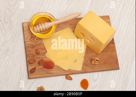 Morceau de fromage et tranches de fromage sur une planche en bois avec miel, noix et abricots secs. Vue de dessus Banque D'Images