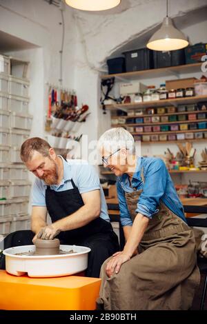 Senior woman spinning clay sur une roue avec une aide d'un professeur de classe de poterie Banque D'Images