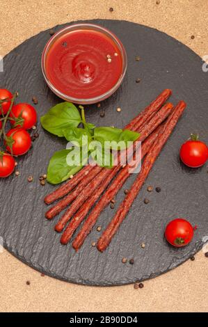 saucisse fine et longue avec sauce, tomates cerises et basilic sur une planche en graphite noir Banque D'Images