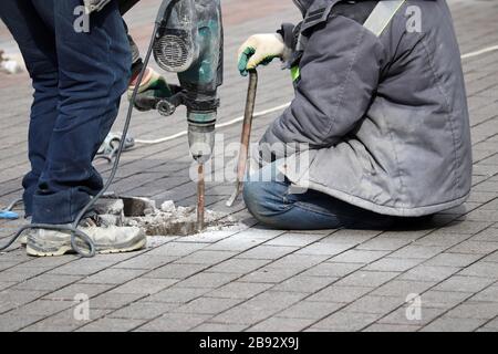 Les travailleurs réparent la surface de la route avec un marteau. Travaux de construction, pose de dalles de revêtement Banque D'Images