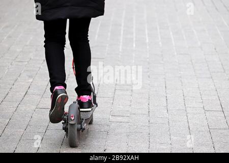 Une fille conduit un scooter électrique sur une rue de la ville, jambes dans des baskets sur un trottoir. Conduite du scooter électronique au printemps Banque D'Images