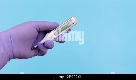 Détail de la main dans des gants médicaux bleus avec un thermomètre sur fond bleu avec espace de copie pour le texte. Protection contre le coronavirus, concept Covid-19. Banque D'Images