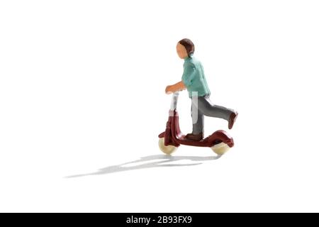 Figurine miniature d'un enfant qui tourne sur un scooter avec ombre sur un fond blanc avec espace de copie Banque D'Images
