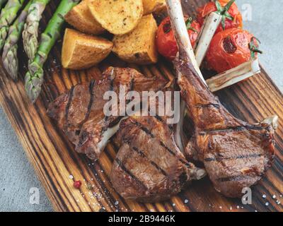 Côtelettes d'agneau grillées sur un panneau en bois avec asperges, sauce rouge, pommes de terre Banque D'Images