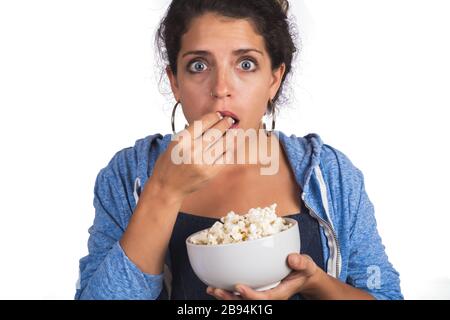 Portrait de la jeune femme qui a peur tout en regardant un film et en mangeant du pop-corn en studio. Arrière-plan blanc isolé. Banque D'Images