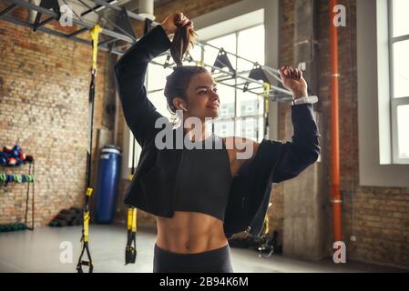 Se sentir heureuse positive et attrayante jeune femme dans un casque écoutant de la musique et souriant tout en faisant de l'exercice à la salle de gym. Le bonheur. Concept sportif. Motivation Banque D'Images