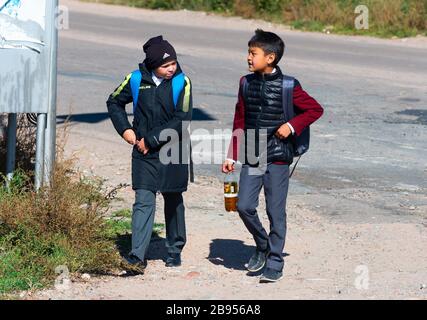 Deux jeunes Kirghizes marchant de l'école portant des vêtements froids et un sac à dos. Enfants en milieu rural au Kirghizstan près de Karakol dans la région d'Issyk Kul. Banque D'Images