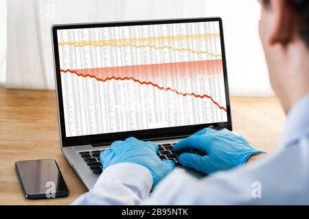 Homme en gants Vérification des graphiques des stocks pendant la collision de la bourse de Coronavirus Banque D'Images