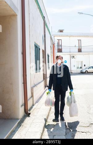 Rue vide, un homme retourne à la maison avec des achats de shopping portant des masques de protection et des gants pour contenir la propagation du coronavirus, Italie dur Banque D'Images