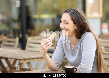 Heureuse jeune femme tenant un snack-bar à céréales assis sur une terrasse de café Banque D'Images