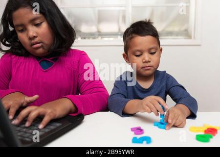 Les enfants à la maison d'apprentissage, avec la sœur plus âgée taper sur un ordinateur portable tandis que son petit frère joue avec des manipulations colorées de nombre. Banque D'Images