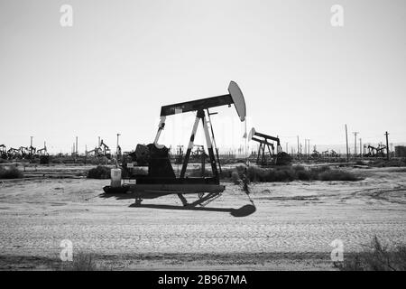 Pompes à huile noir et blanc fonctionnant dans le désert ensoleillé de Californie. Ces crics peuvent extraire 5 à 40 litres d'émulsion de pétrole brut et d'eau à chaque passage. Banque D'Images