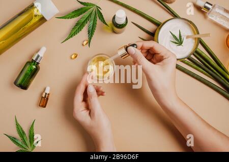 Pipeter avec de l'huile cosmétique CBD dans les mains des femmes sur un fond de table avec des cosmétiques avec du cannabis et des feuilles de marijuana Banque D'Images