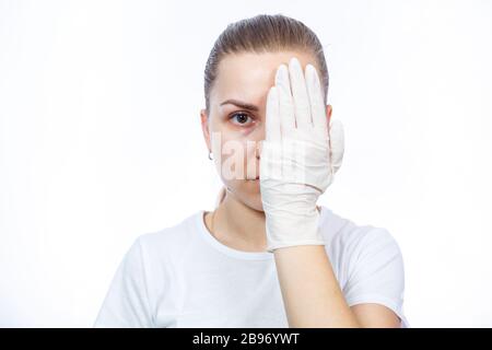 Fille paramédic met des gants médicaux blancs sur les mains. Protection contre les germes et les virus. Elle est dans un T-shirt blanc sur un fond blanc. Banque D'Images