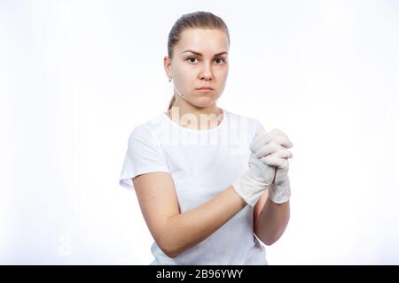 Fille paramédic met des gants médicaux blancs sur les mains. Protection contre les germes et les virus. Elle est dans un T-shirt blanc sur un fond blanc. Banque D'Images